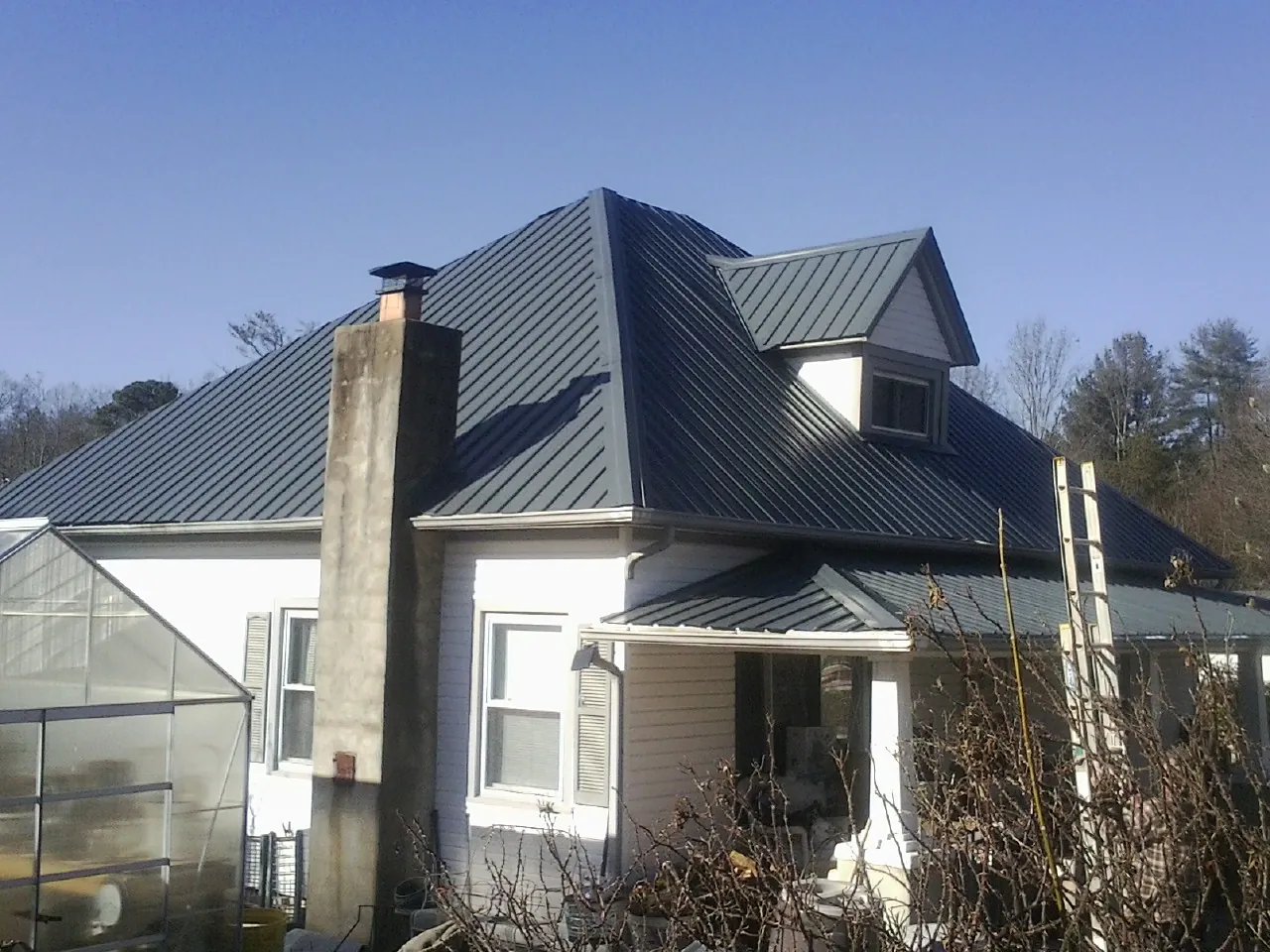Dark blue standing seam metal roof on a white farmhouse with dormer — Slate & Tile Roof Repair by Roofing Brothers in Koppel