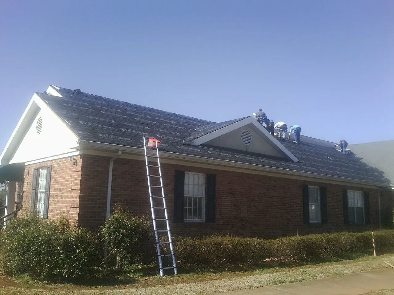 Crew tearing shingles off a brick ranch roof with a ladder set — Metal Roof Repair work by our crew in Koppel