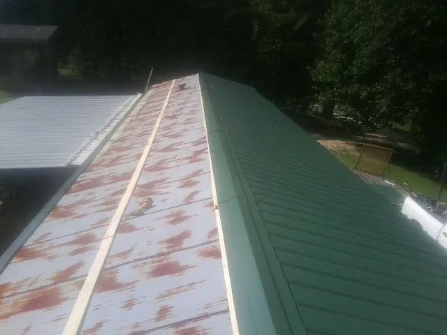 Old rusted panels beside newly installed green metal roofing — Wind Damage Roof Repair by Roofing Brothers in Koppel