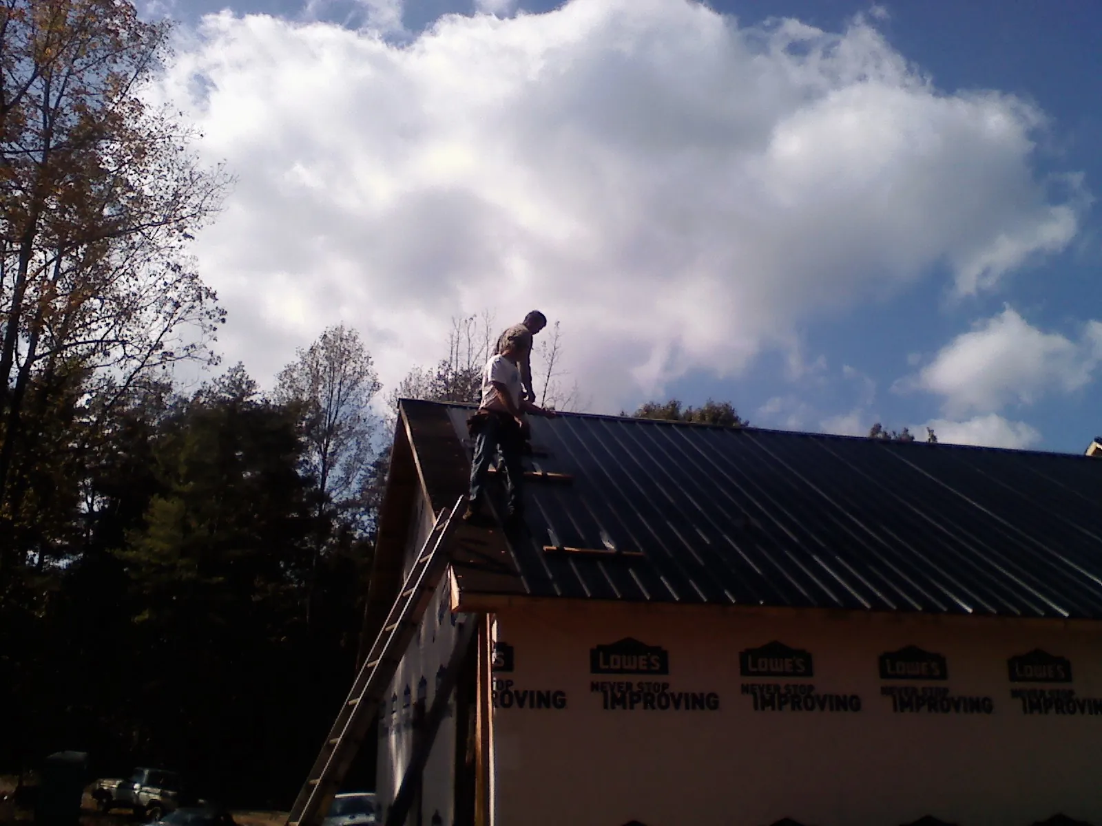 Roofer fastening dark metal panels high against a cloudy sky, from a Roof Inspection job in Koppel