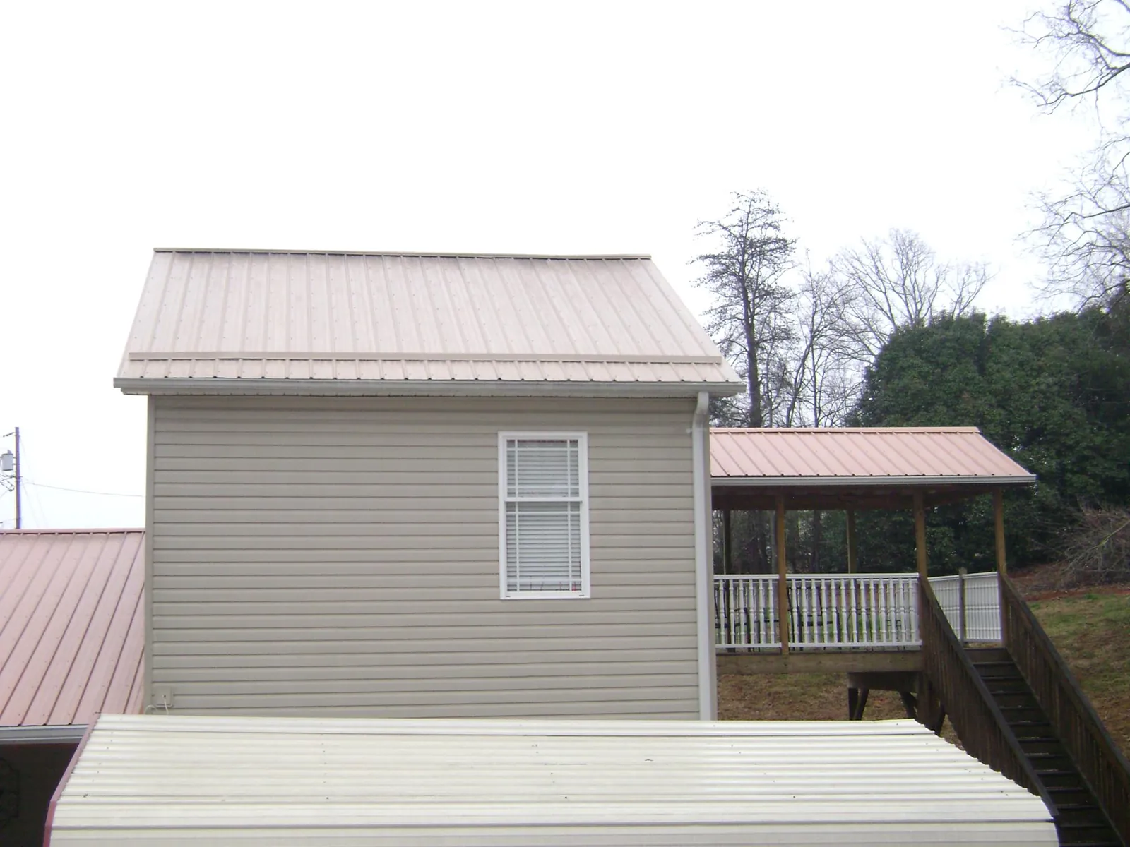 Tan metal roofs on a two story addition and attached porch, from a Roof Replacement job in Koppel